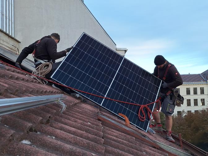 Zwei Arbeiter montieren eine Solarplatte auf einem Dach.