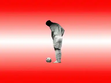 Ein Fußballspieler steht auf einem rot-weißen Hintergrund, den Kopf gesenkt, vor einem Ball.