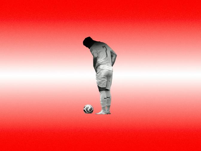 Ein Fußballspieler steht auf einem rot-weißen Hintergrund, den Kopf gesenkt, vor einem Ball.
