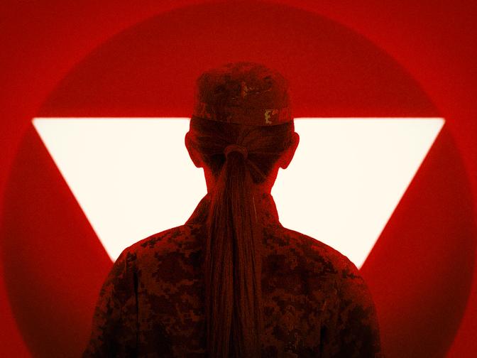 Silhouette einer Person in Tarnuniform vor einem roten Hintergrund mit einem auffälligen weißen Dreieck.