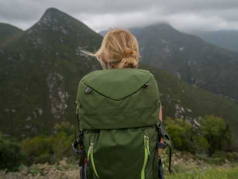 Eine Frau mit einem Rucksack steht vor einem Bergpanorama.