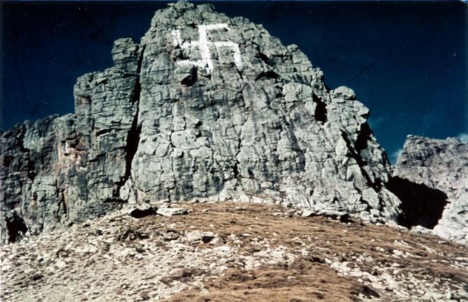 Eine felsige Klippe, auf deren Oberfläche ein großes weißes Hakenkreuz gemalt ist, vor einem strahlend blauen Himmel.
