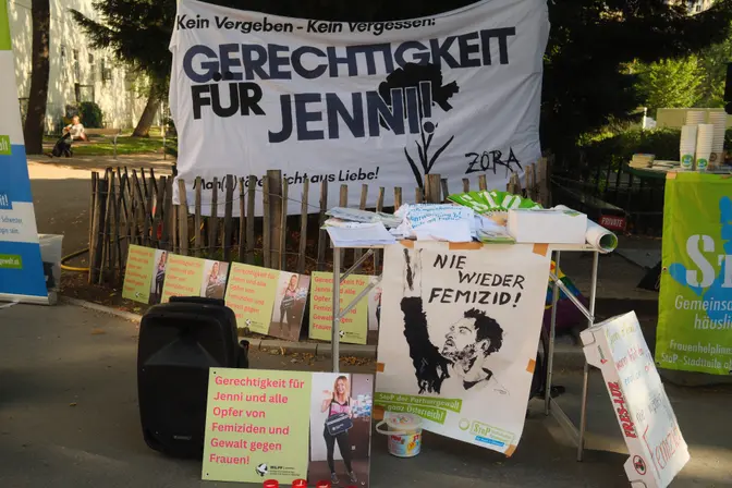 Protestaktion mit Plakaten für Gerechtigkeit gegen Femizid, Banner mit "Gerechtigkeit für Jenni" und Infotisch auf der Straße.