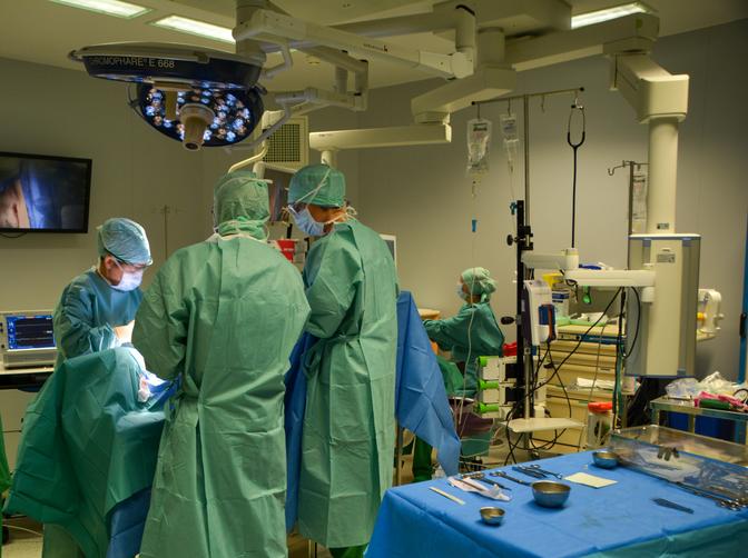 Surgeons in an operating room performing surgery, surrounded by medical equipment and bright lights.