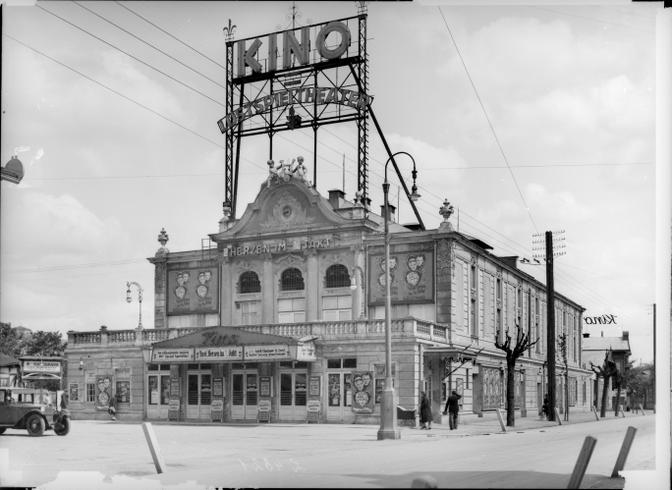 Historisches Kino im Wiener Prater mit reich verzierten Fassaden und Werbeschildern, im Vordergrund Straßenlaternen und ein geparktes Auto.